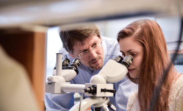 A man looking at a woman who is looking through a microscope.
