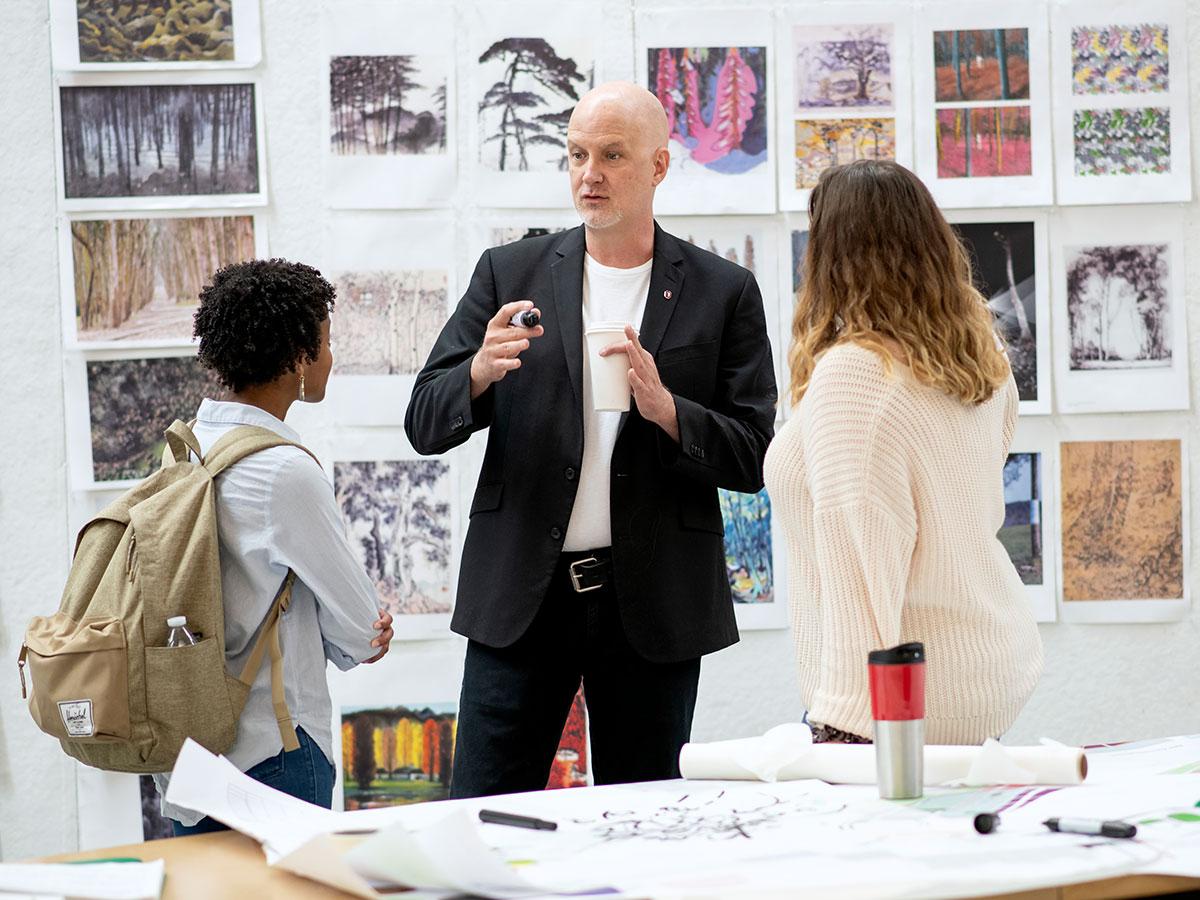 A man is standing and talking while two women listen